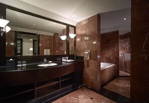 A modern bathroom with a large mirror, dark marble walls, a sink, and a bathtub.