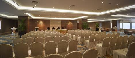 A conference room with rows of chairs, a stage with a podium, and a large window providing a view.