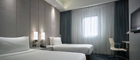 A hotel room with two beds, a desk, a chair, and a TV.