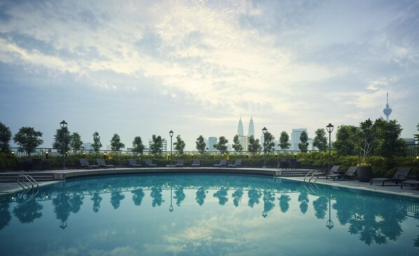 A swimming pool with lounge chairs and a view of a city skyline in the background.