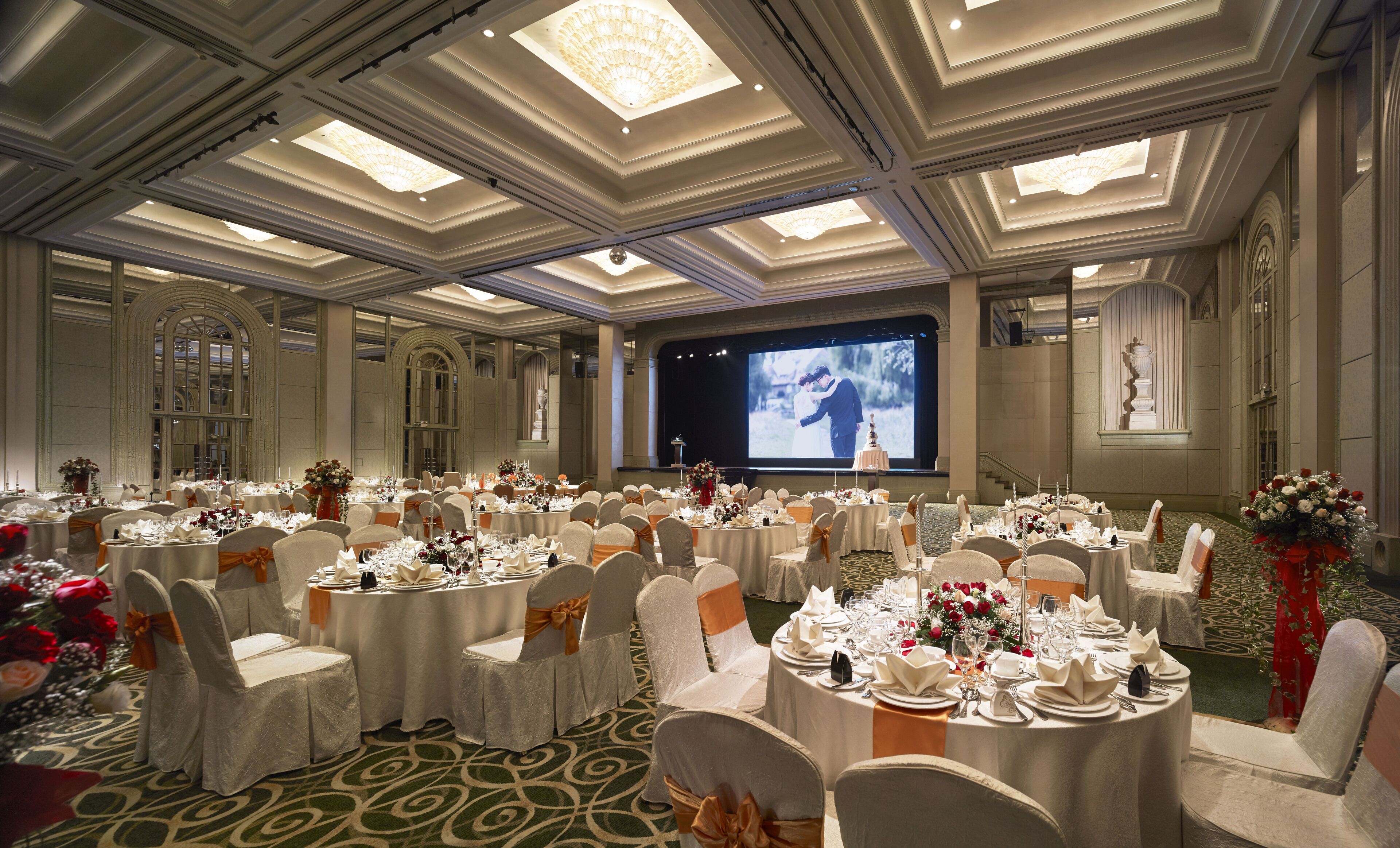 A banquet hall with round tables, white chairs, and a large screen for presentations.