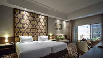 A hotel room with a large bed, a desk, a chair, and a view of the city through the window.