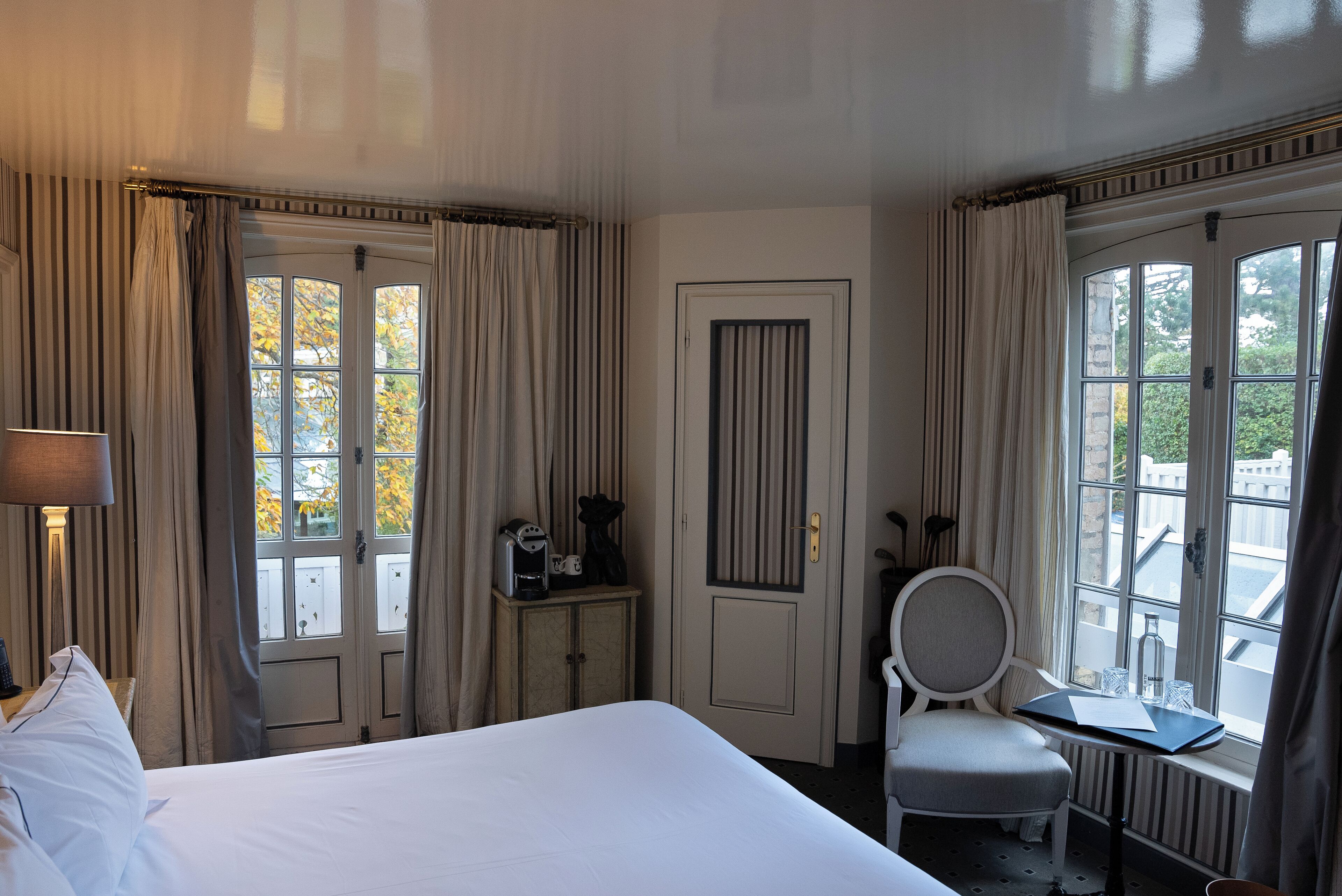 Ett hotellrum med en stor säng, ett skrivbord med en stol, ett fönster med gardiner och en dörr.