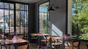 Un restaurant doté de grandes fenêtres, de chaises en osier et de tables dressées pour le service.