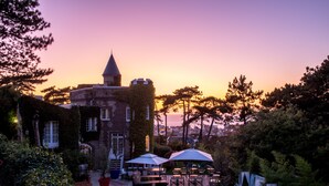 Un bâtiment qui ressemble à un château, doté d’une piscine, d’un espace extérieur aménagé et offrant une vue sur le coucher de soleil.