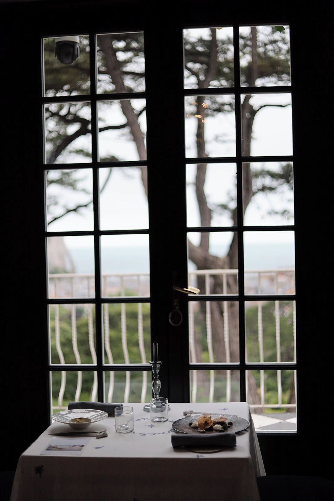 Mesa lista para comer con vistas a árboles y un cuerpo de agua a través de una ventana con diseño de cuadrícula.