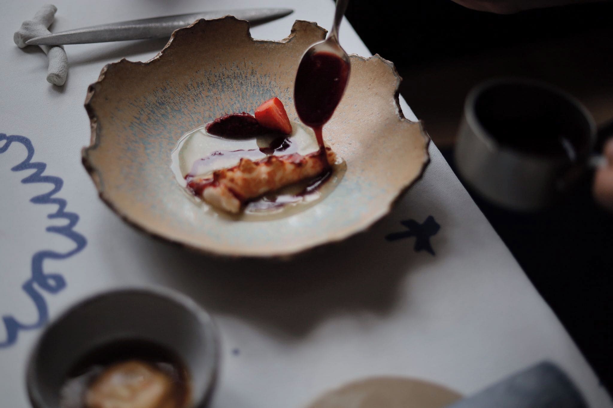 Une assiette contenant un morceau de nourriture et une cuillère de sauce, un couteau et une tasse, le tout posé sur une table.