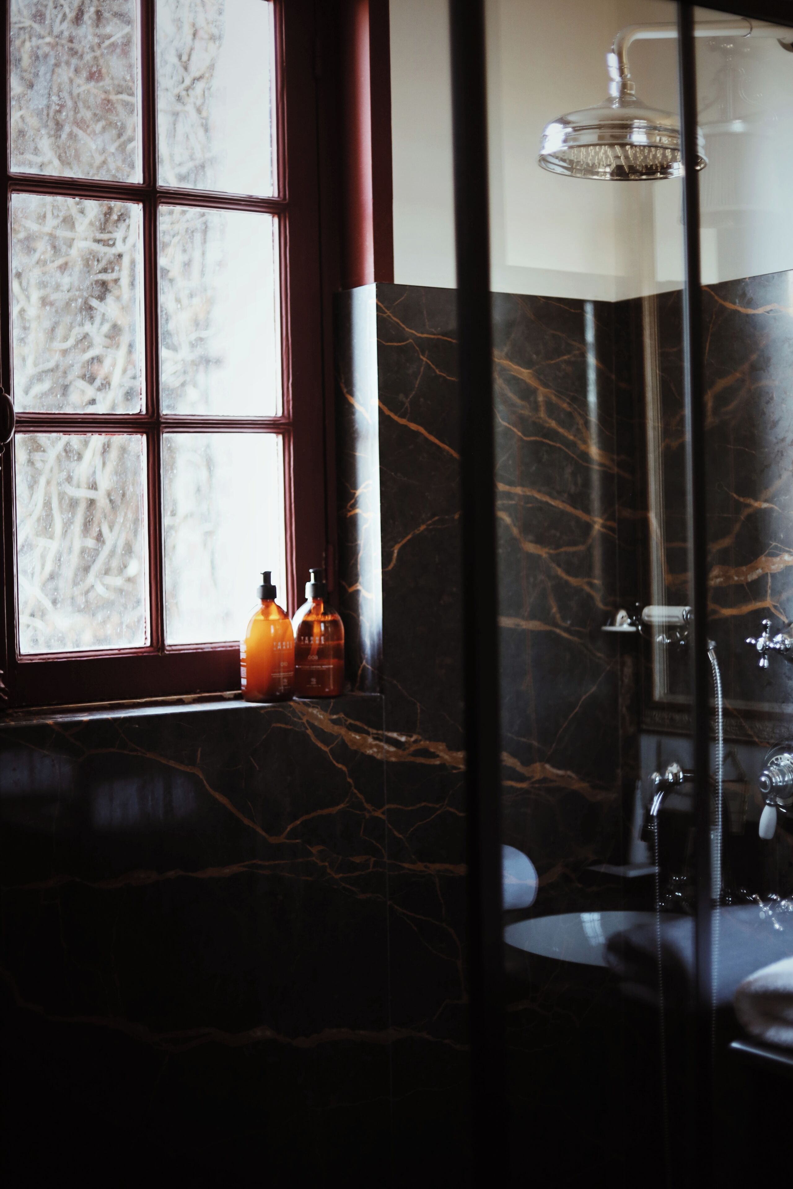 A bathroom with a large window, a bathtub, and two bottles on the windowsill.