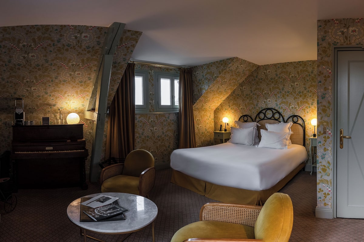 A hotel room with a bed, a desk, a chair, a small table, and a door.