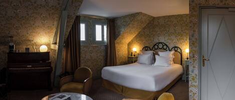 A hotel room with a bed, a desk, a chair, a small table, and a door.