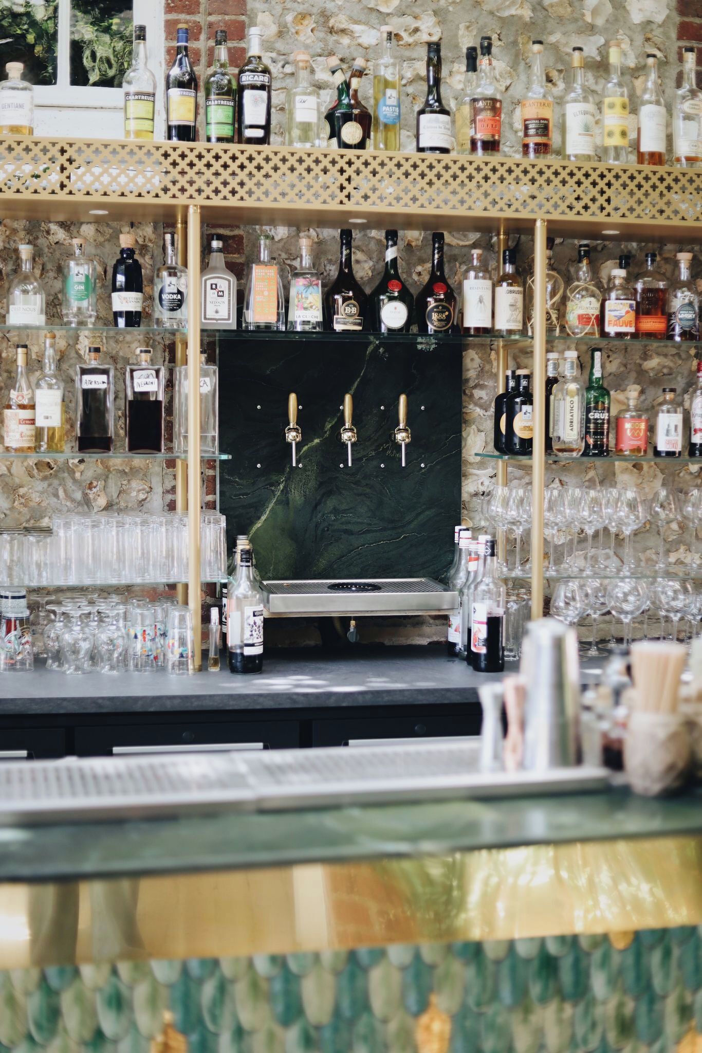 A bar area with a marble wall, shelves of liquor bottles, a tap system, and glasses.