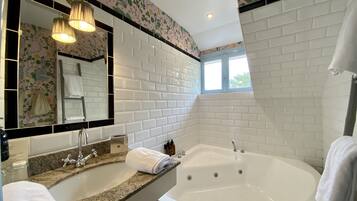 A bathroom with a large bathtub, a sink, a mirror, and a window.