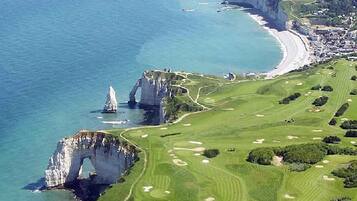 An aerial view of a coastal golf course with a distinctive cliff formation and a beach.