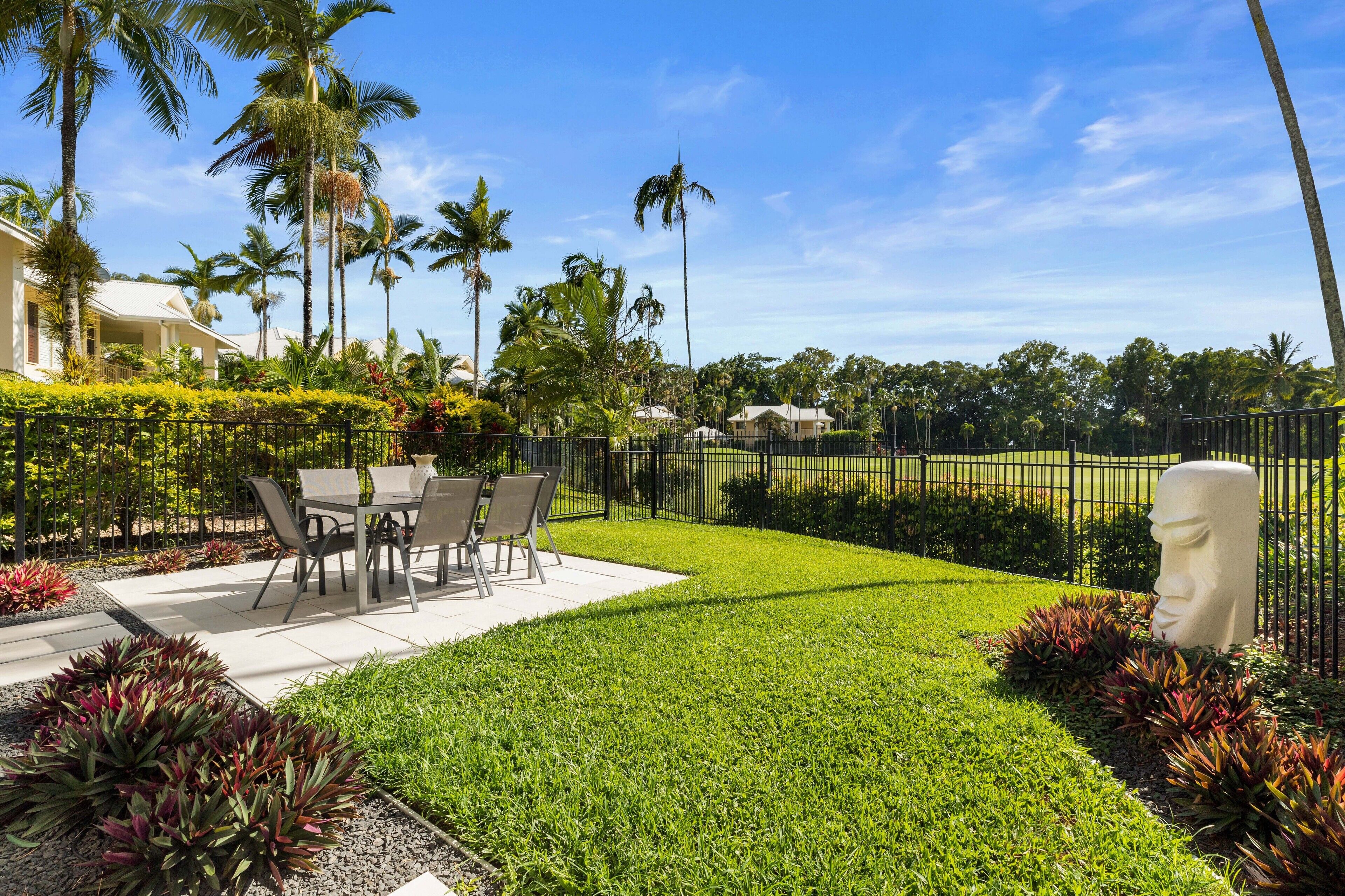 A well-maintained outdoor patio area with a dining table and chairs, surrounded by lush greenery and palm trees.