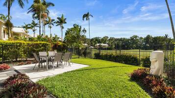 A well-maintained outdoor patio area with a dining table and chairs, surrounded by lush greenery and palm trees.