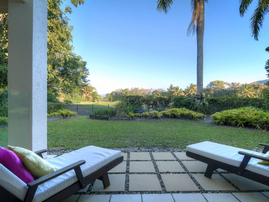A patio with two lounge chairs and a view of a well-maintained garden and distant hills.