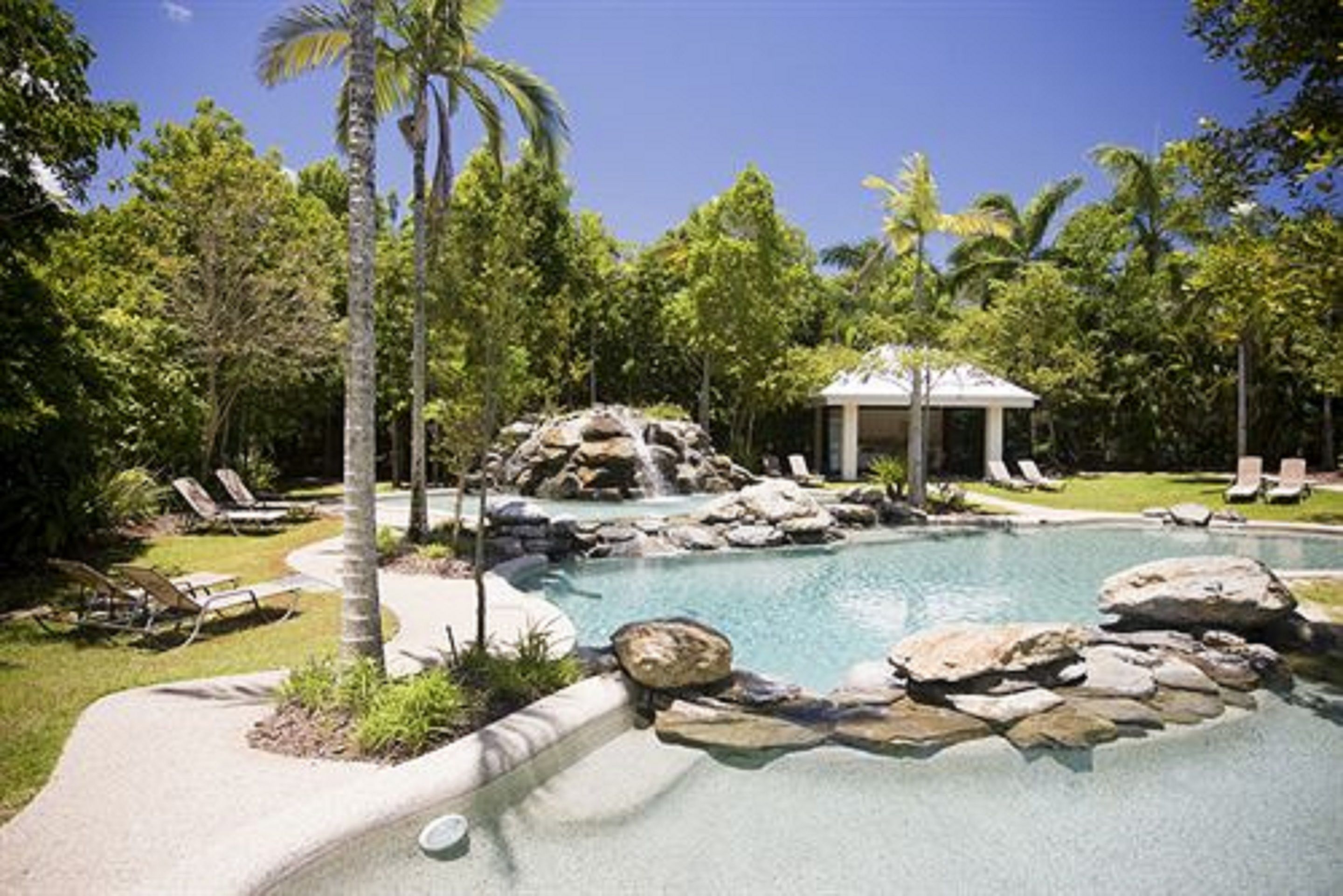 A pool with a waterfall, surrounded by palm trees and lounge chairs.