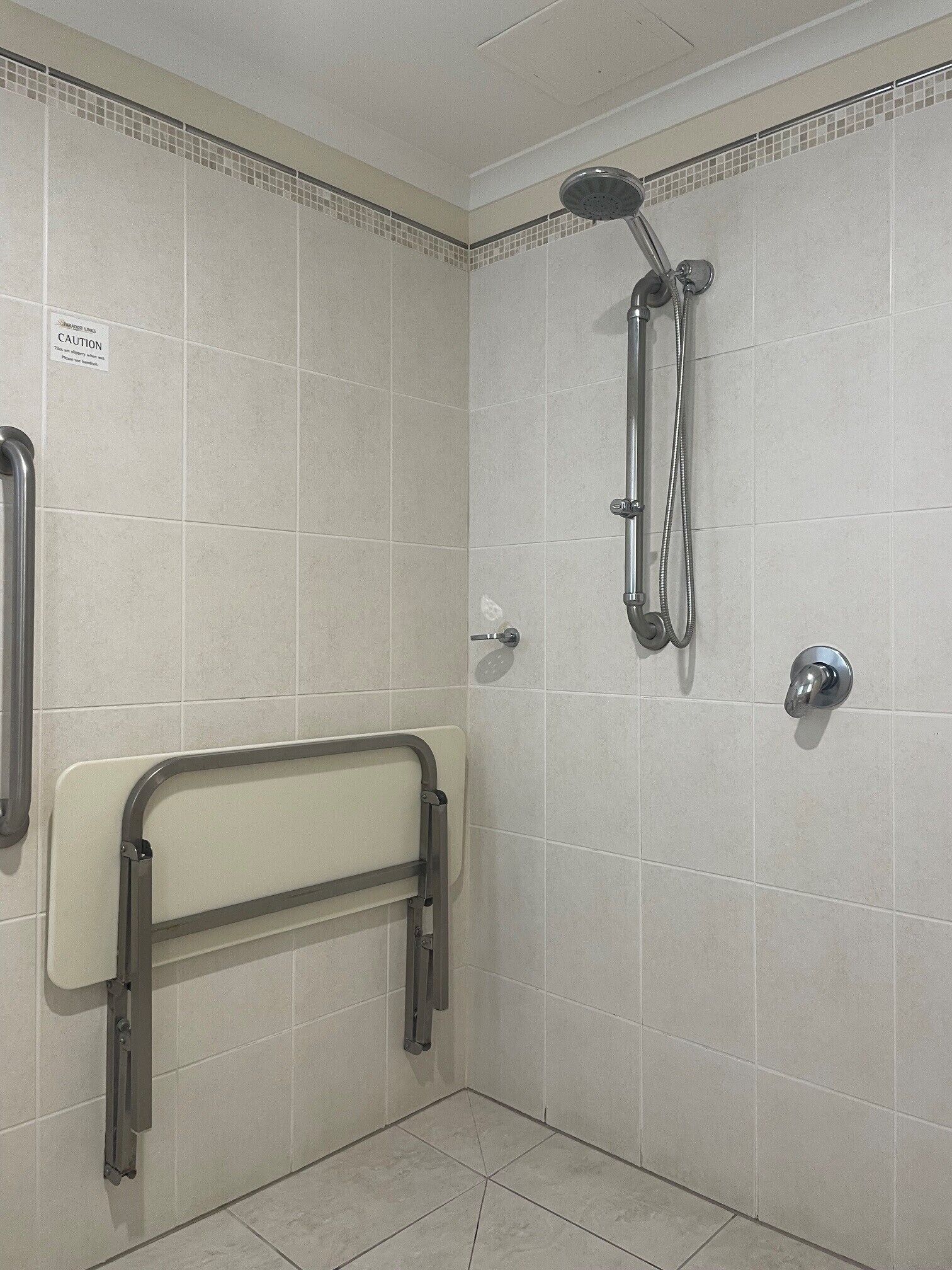 A bathroom with a shower, grab bar, and tiled walls.