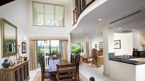 A spacious dining area with a high ceiling and large windows, a kitchen with a modern design, and a view of greenery outside. - Paradise Links Resort Port Douglas (Craiglie)