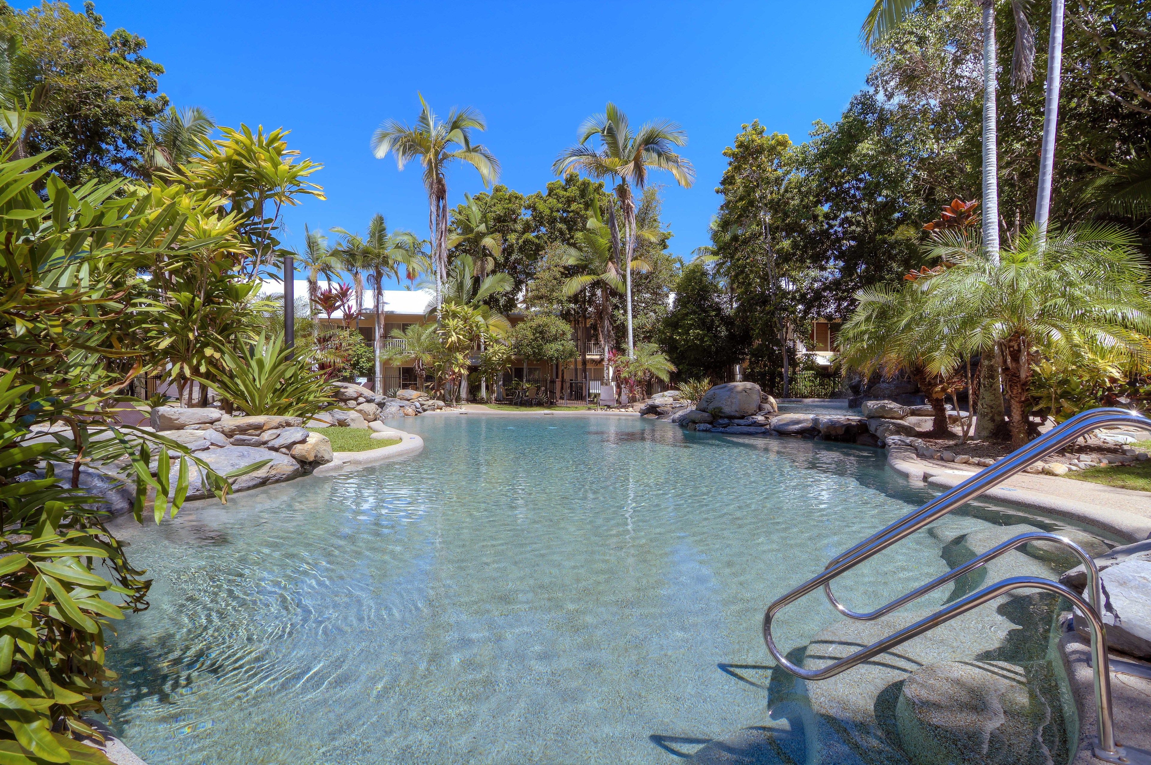 A clear pool surrounded by tropical plants and rocks, with a metal ladder leading into the water.