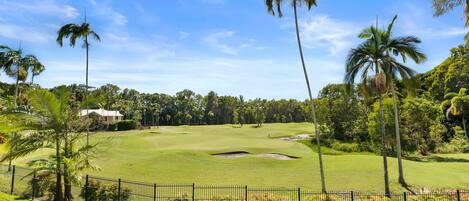 A golf course with a fence, palm trees, and a building in the background.