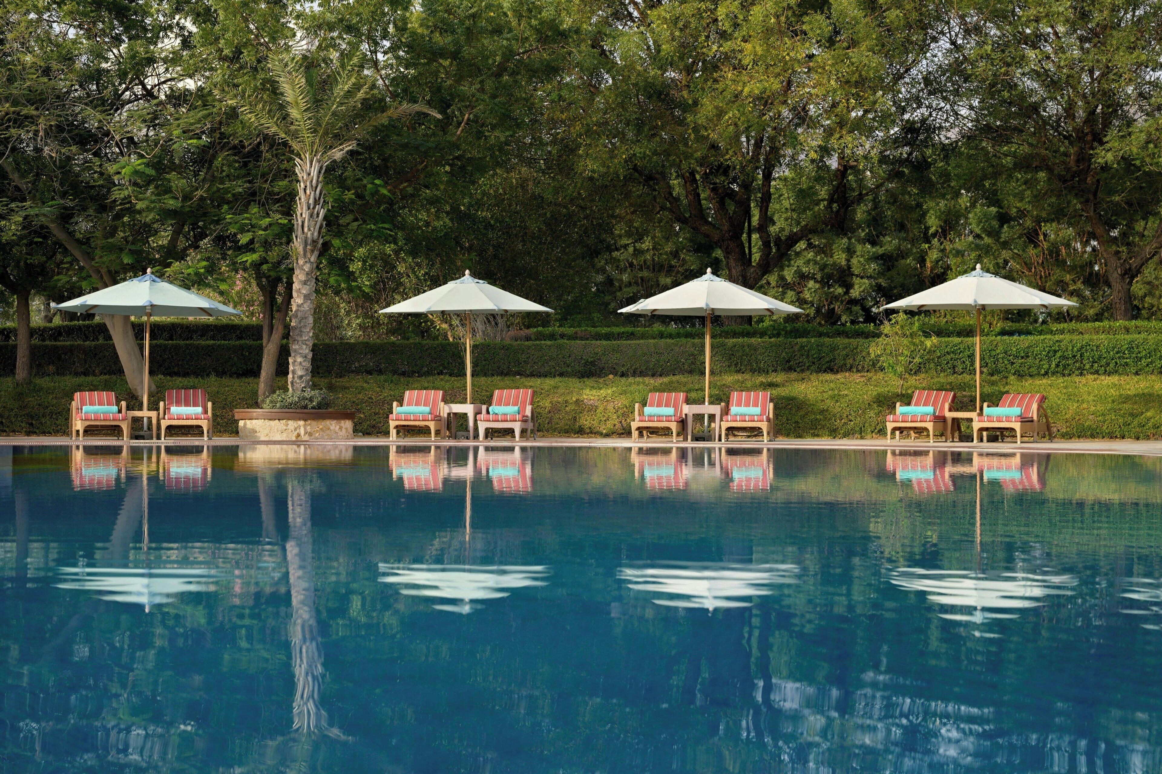 A swimming pool with lounge chairs and umbrellas, surrounded by trees.