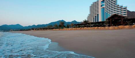 Un hotel frente a la playa con diseño moderno, que cuenta con un edificio grande con varios balcones y un patio frente a la playa.