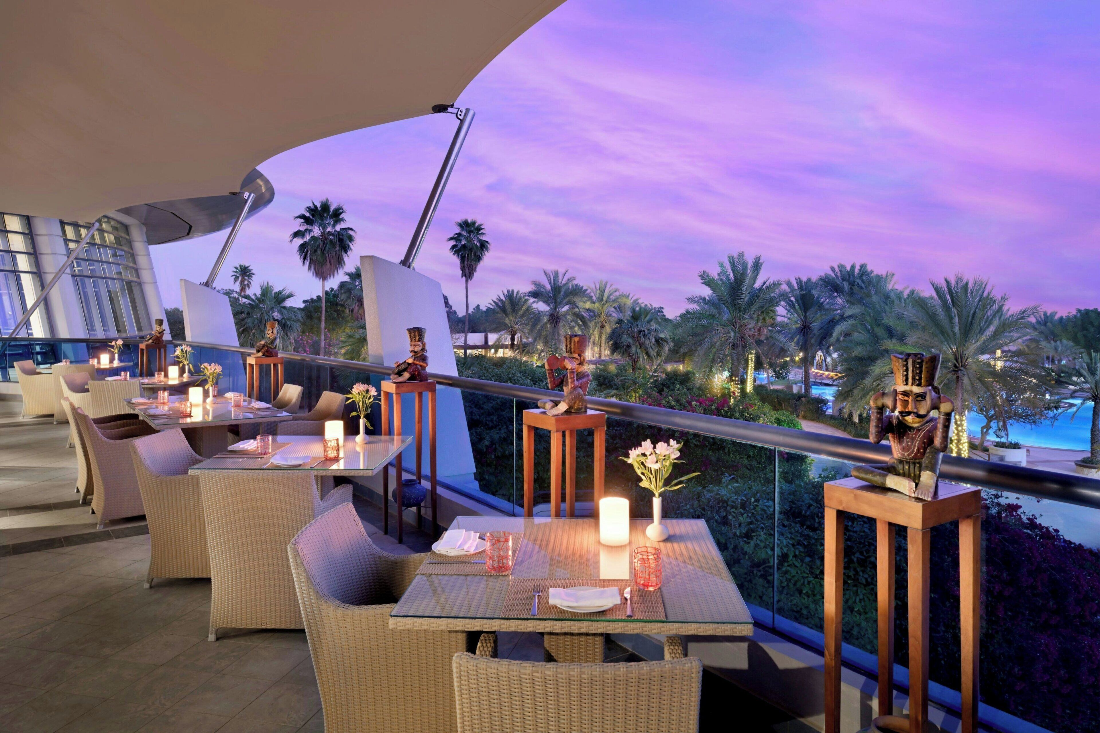 A rooftop dining area with wicker furniture, candles, and decorative statues.