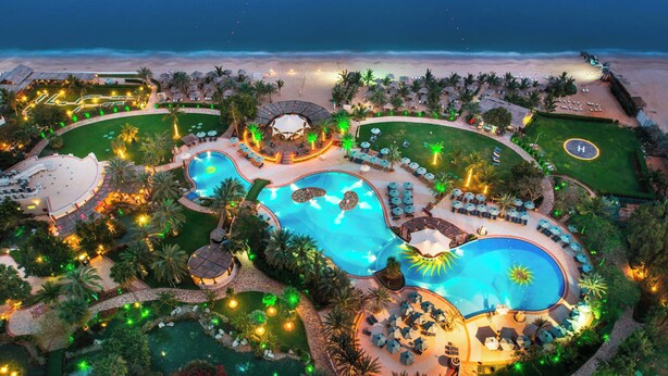 A resort with multiple swimming pools, a beach, and a well-lit outdoor area.