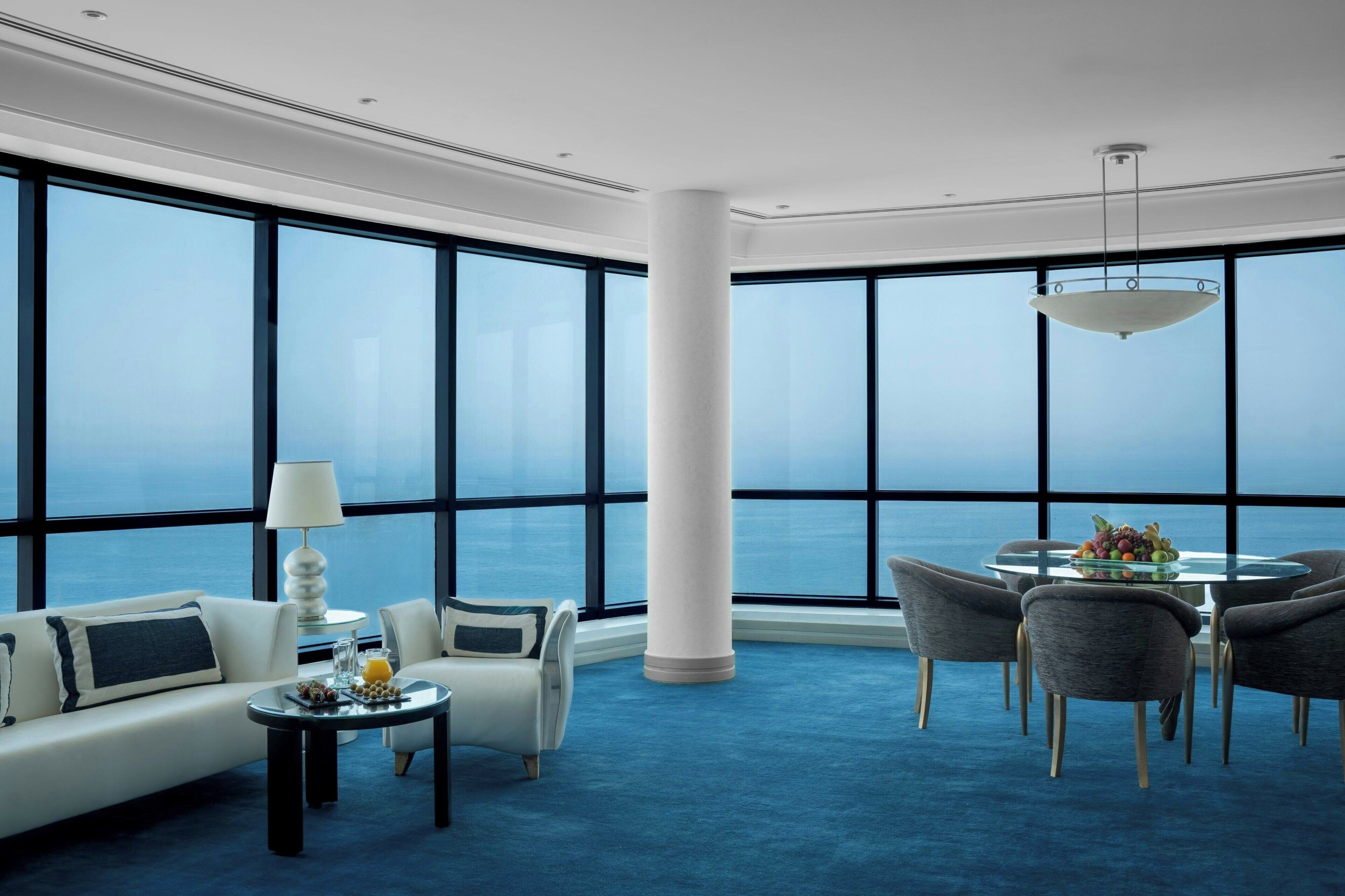 Una habitación de hotel moderna con un ventanal grande, una mesa redonda para comer y un sofá.