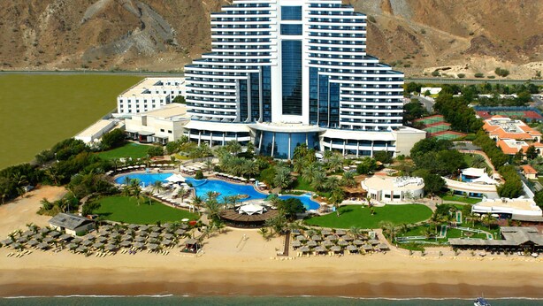 A large hotel with a central swimming pool, multiple balconies, and a beach area with sun loungers. - Le Meridien Al Aqah Beach Resort (Al Aqah)