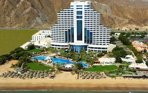 A large hotel with a central swimming pool, multiple balconies, and a beach area with sun loungers. - Le Meridien Al Aqah Beach Resort (Al Aqah)