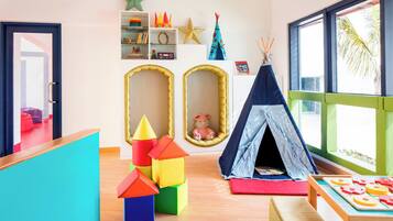 Une salle de jeux pour enfants avec des blocs de construction colorés, une tente et une fenêtre donnant sur des palmiers.