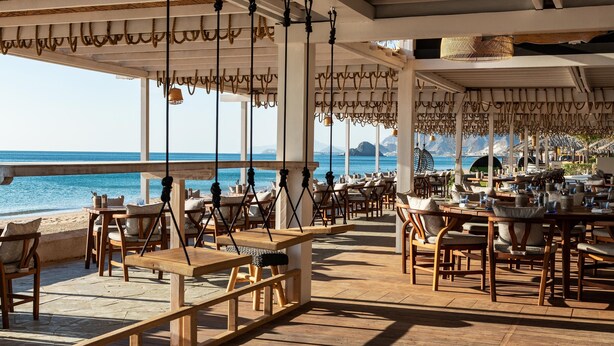 An outdoor dining area with wooden tables and chairs, overlooking the sea. - Le Meridien Al Aqah Beach Resort (Al Aqah)