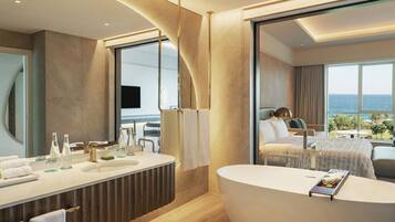 A modern bathroom with a large bathtub, a vanity with a mirror, and a large window offering a view of the sea.