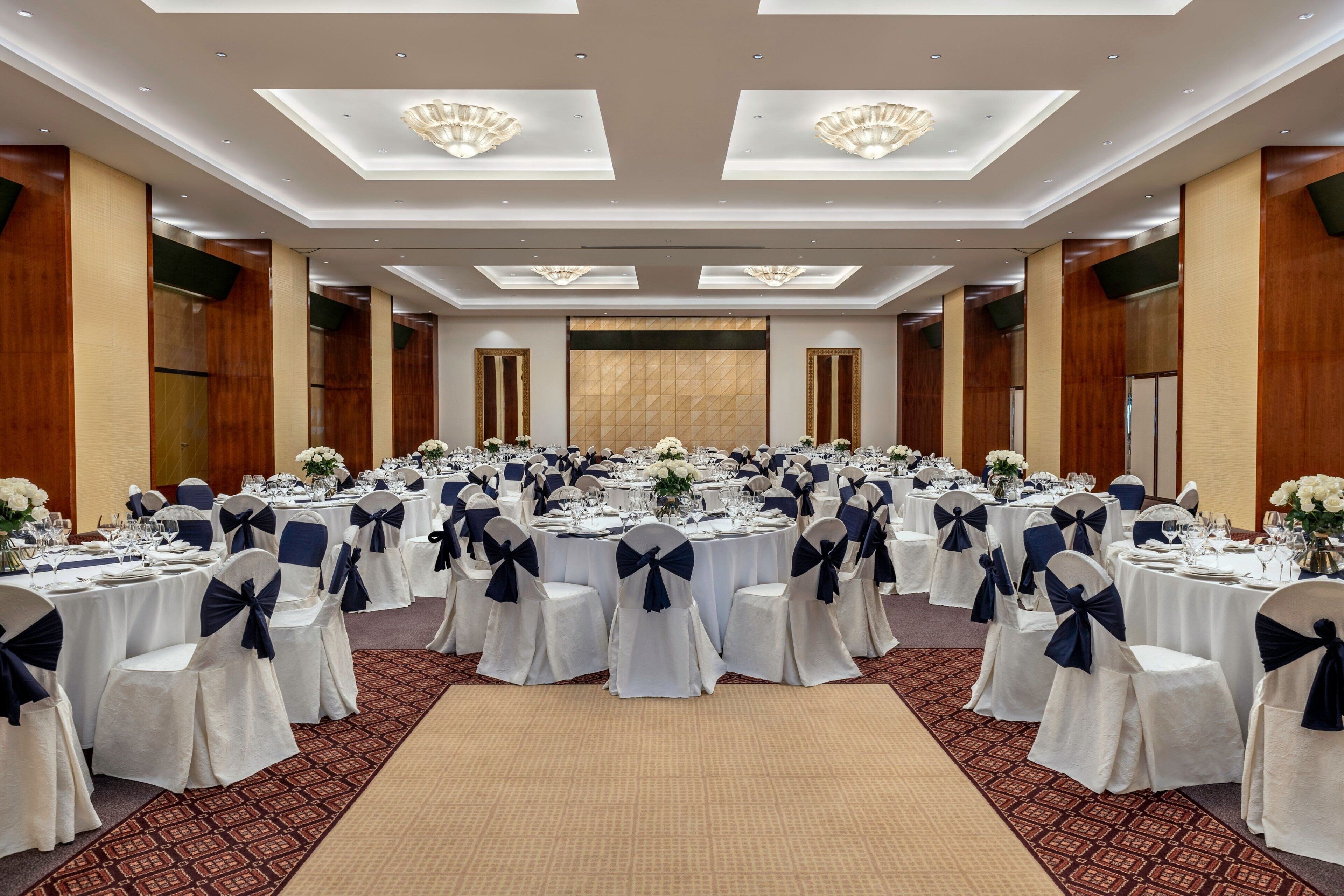 A banquet hall with round tables, white tablecloths, and navy blue chairs.