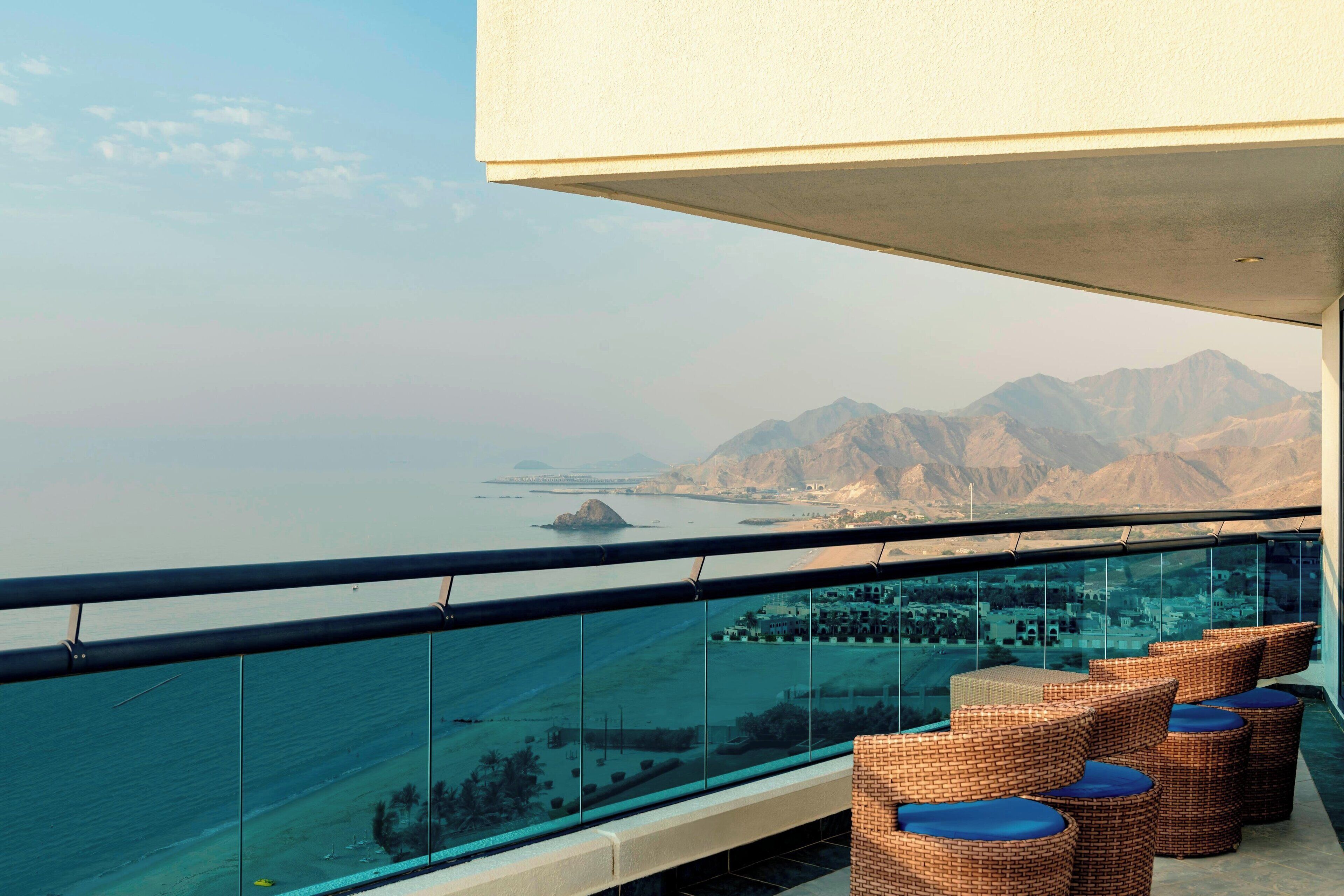 A balcony with wicker furniture and a view of a beach and mountains.