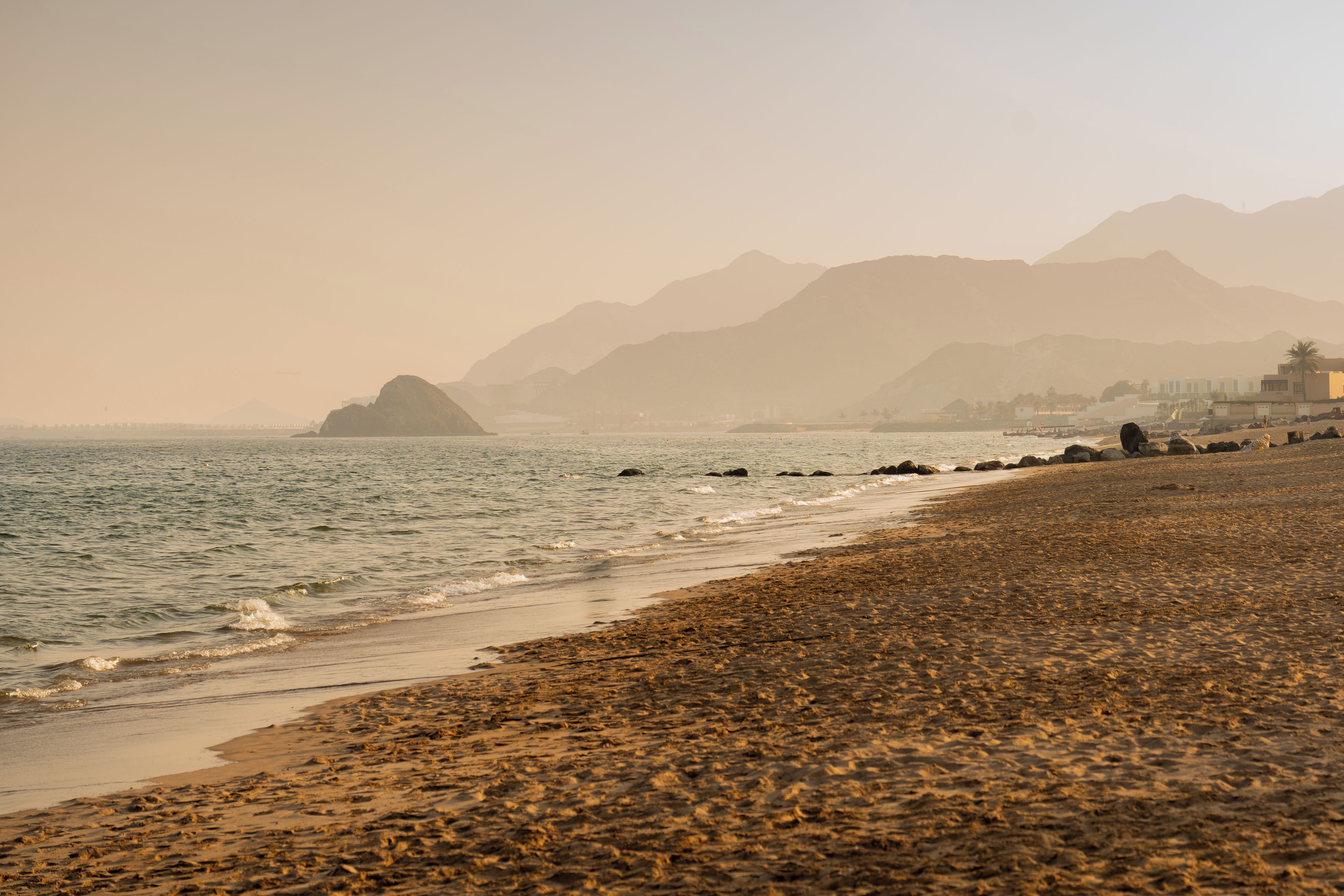 Ein Strand mit felsigem Ufer, ruhiger See und Bergen im Hintergrund.