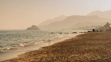Ein Strand mit felsigem Ufer, ruhiger See und Bergen im Hintergrund.