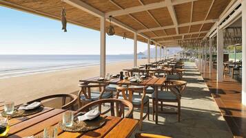 Un área de comedor al aire libre con mesas y sillas, con vista a una playa.