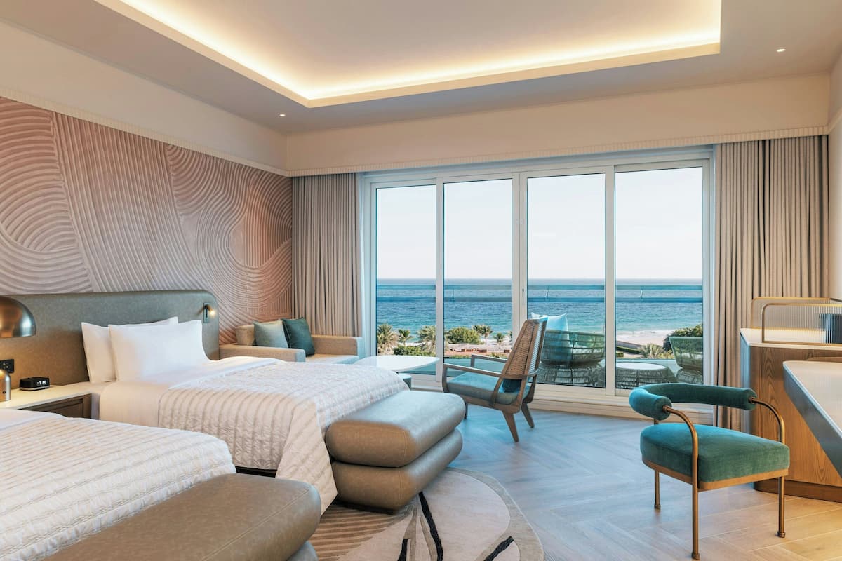 A modern hotel room with a large bed, a sofa, a desk, and a view of the ocean.