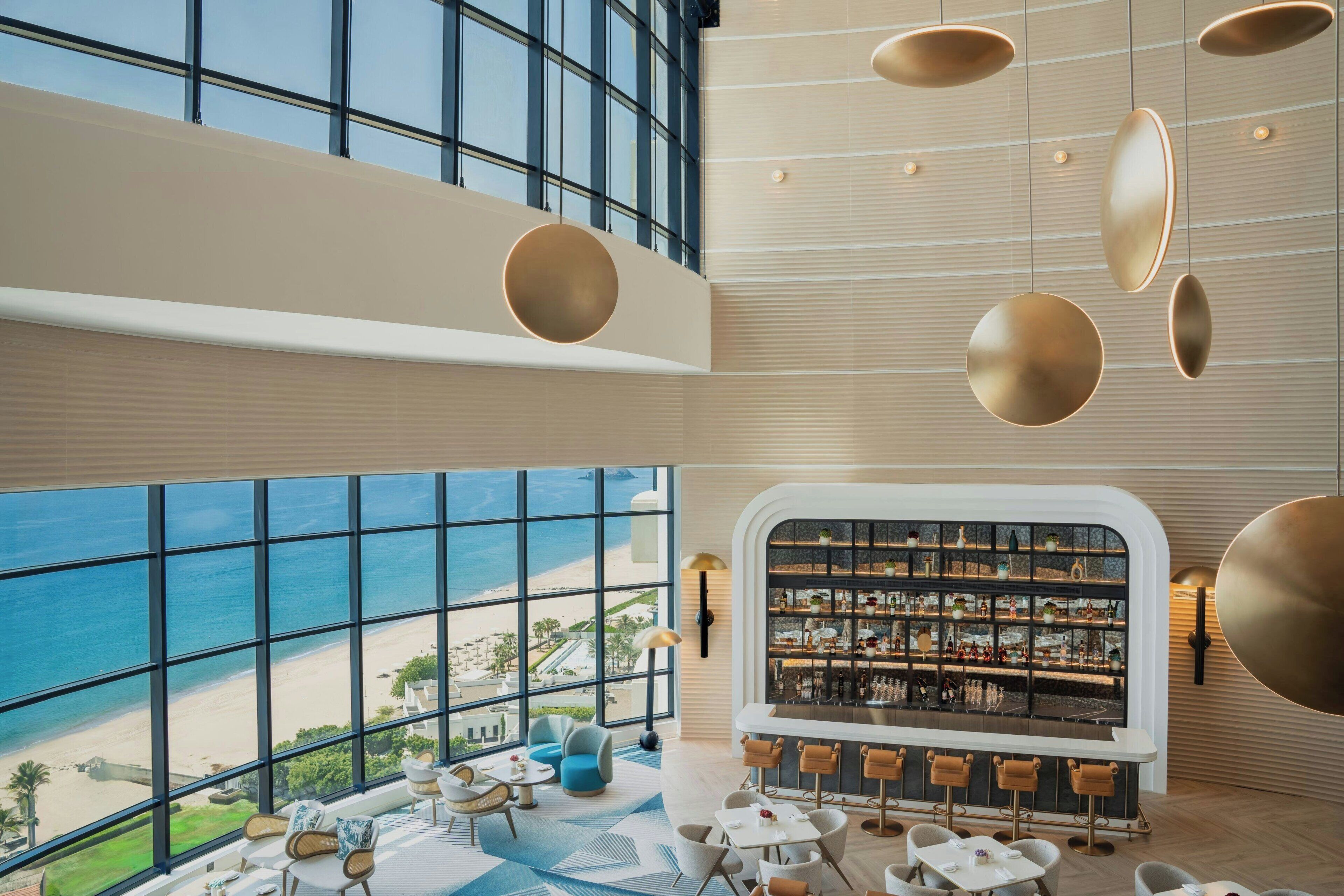 Zona de bar moderna con vistas a la playa, amplios ventanales y mobiliario contemporáneo.