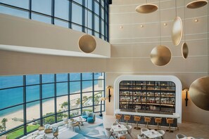 A modern bar area with a view of the beach, large windows, and contemporary furniture. - Le Meridien Al Aqah Beach Resort (Al Aqah)