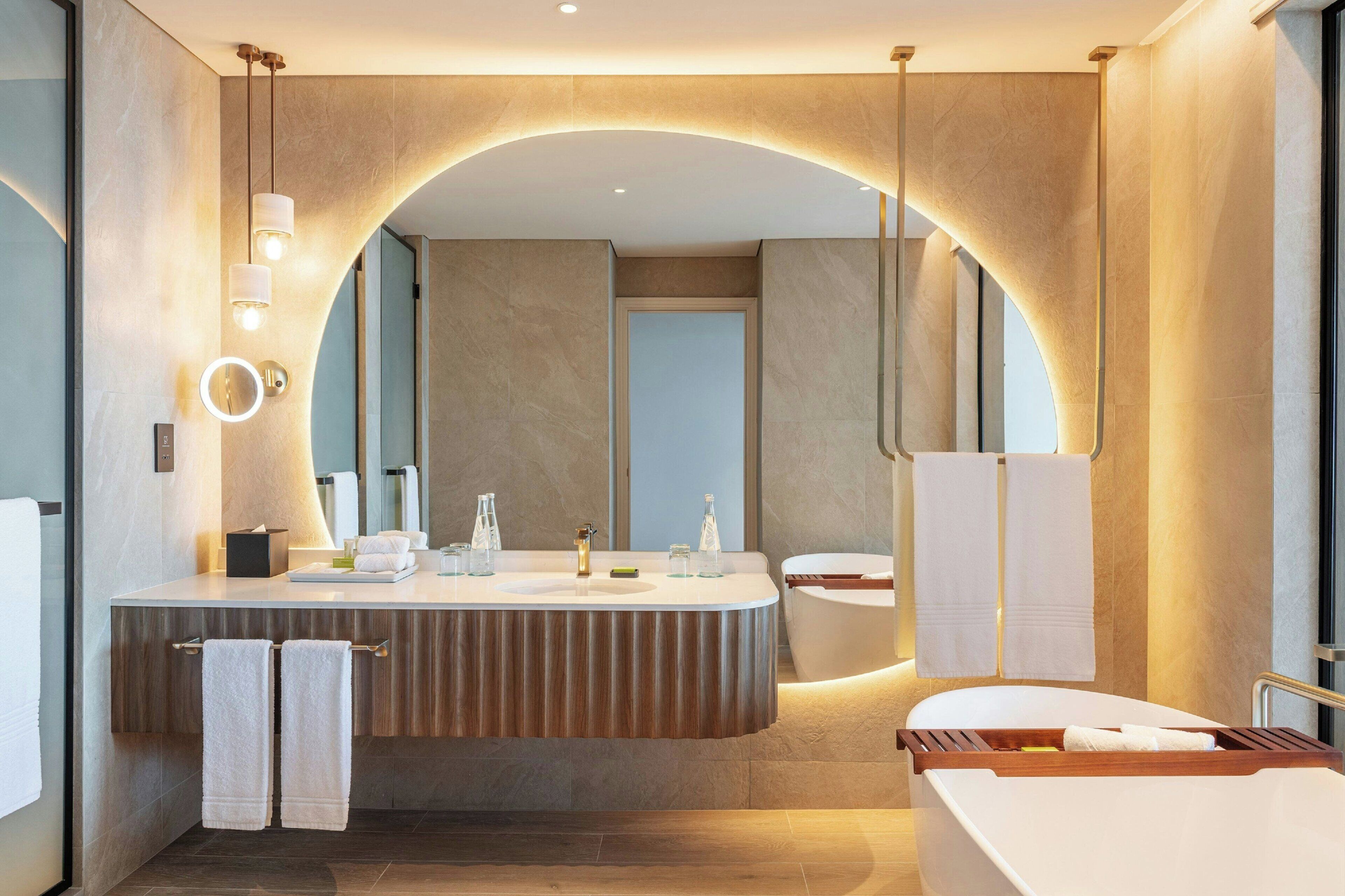 A modern bathroom with a large mirror, a freestanding bathtub, and a vanity with a towel rack.