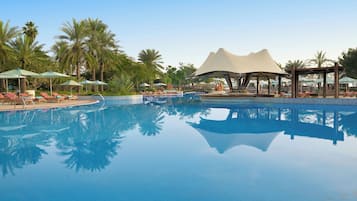 A clear blue pool with lounge chairs and umbrellas, surrounded by palm trees.