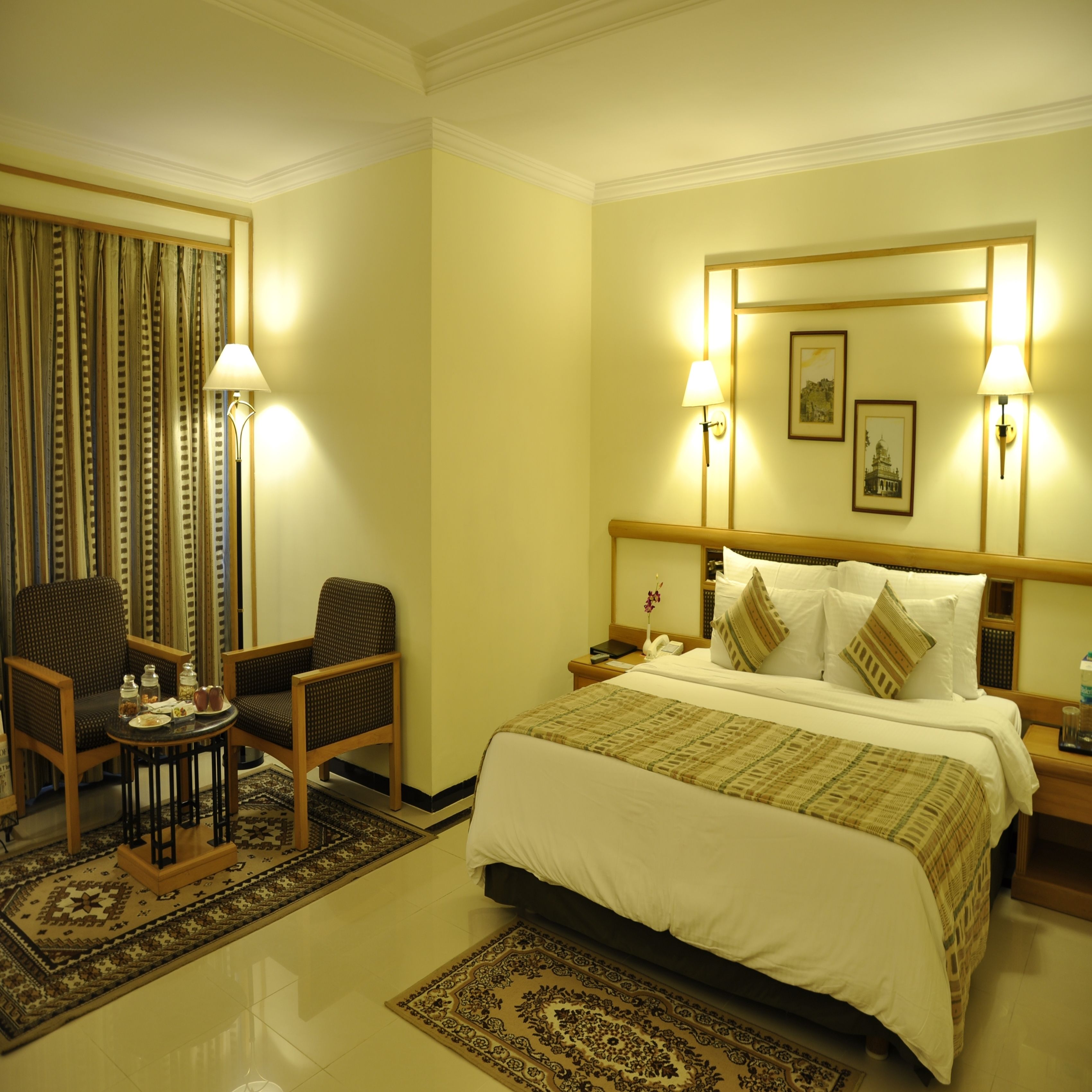 A hotel room with a bed, two chairs, a small table, and a nightstand.
