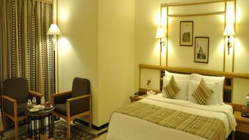 A hotel room with a bed, two chairs, a small table, and a nightstand.