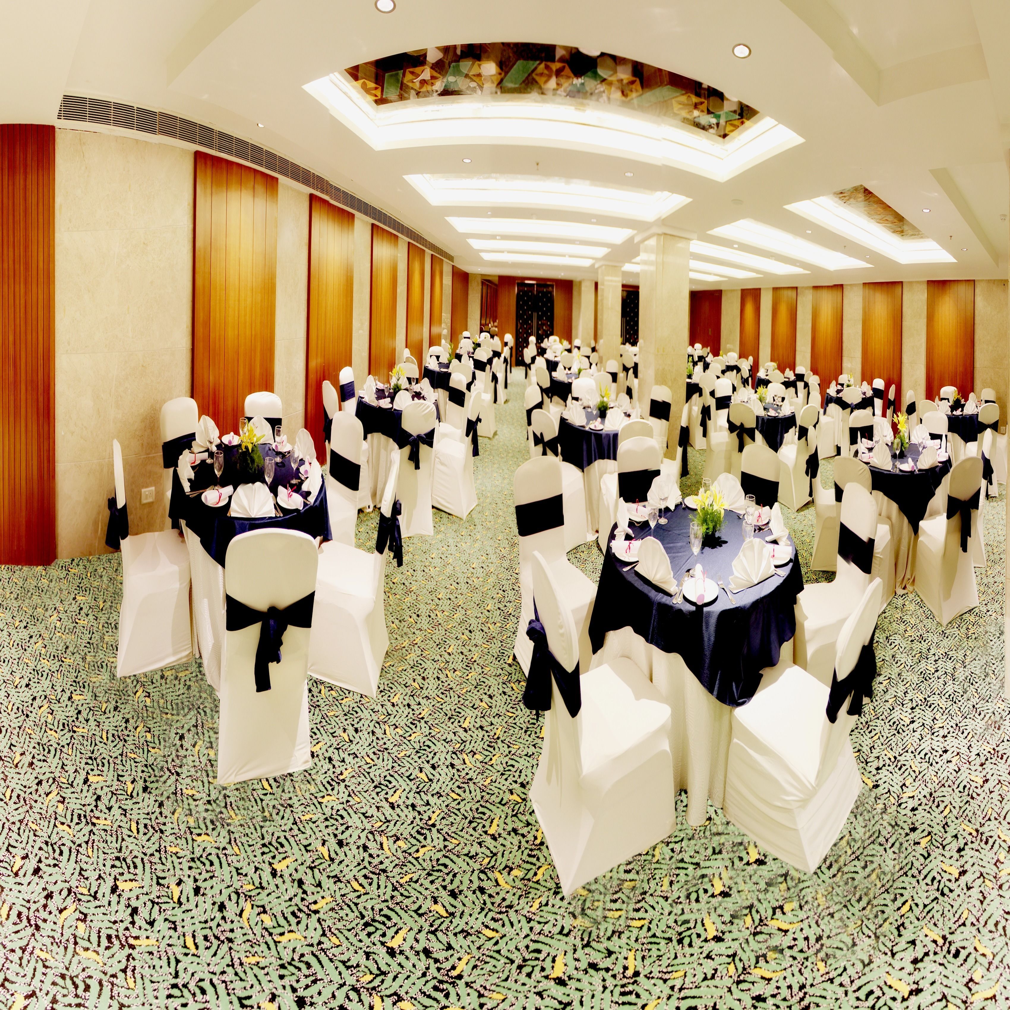 Un salón de banquetes con mesas redondas, sillas blancas y manteles negros.