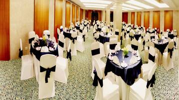 Un salón de banquetes con mesas redondas, sillas blancas y manteles negros.