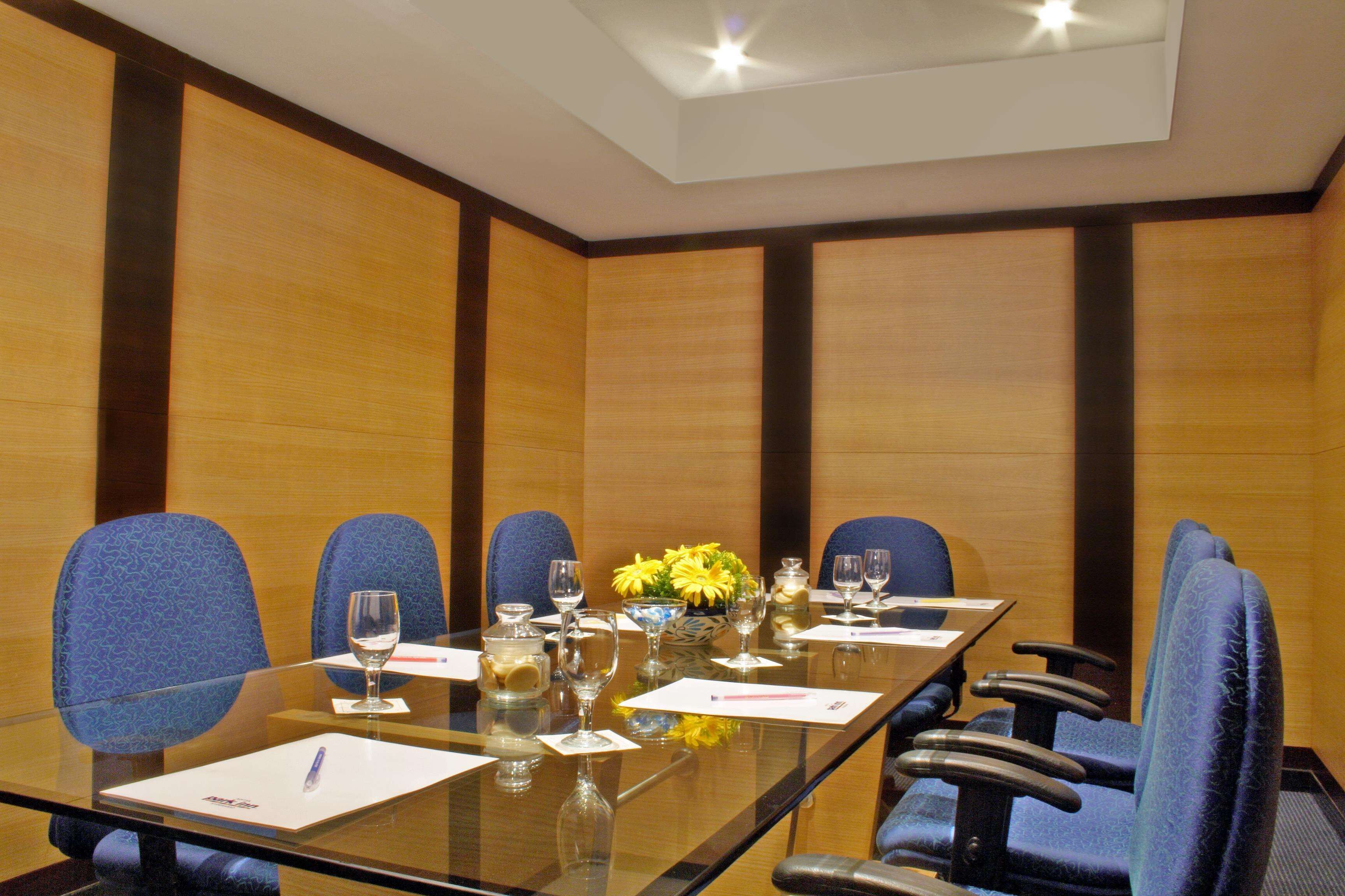 A conference room with a glass table, blue chairs, and a vase of yellow flowers.